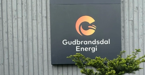 Bilde av logo til Gudbrandsdal Energi på veggen ute med blomster fremfor